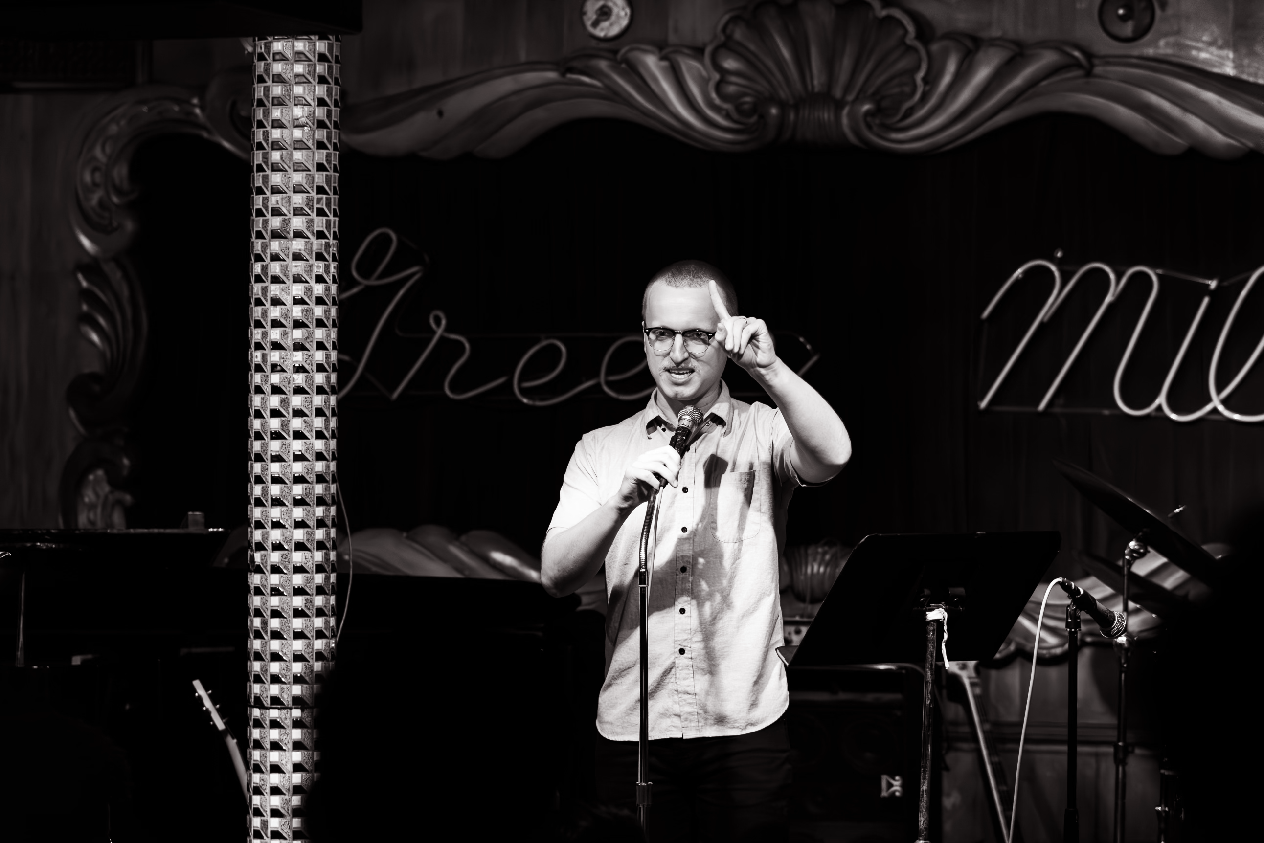 Chicago Comedian Max Walter preforming live on stage during a comedy show at the comedy car, The Green Room, in Chicago, Illinois. Max is mid joke, with this mouth open, and finger in the air.