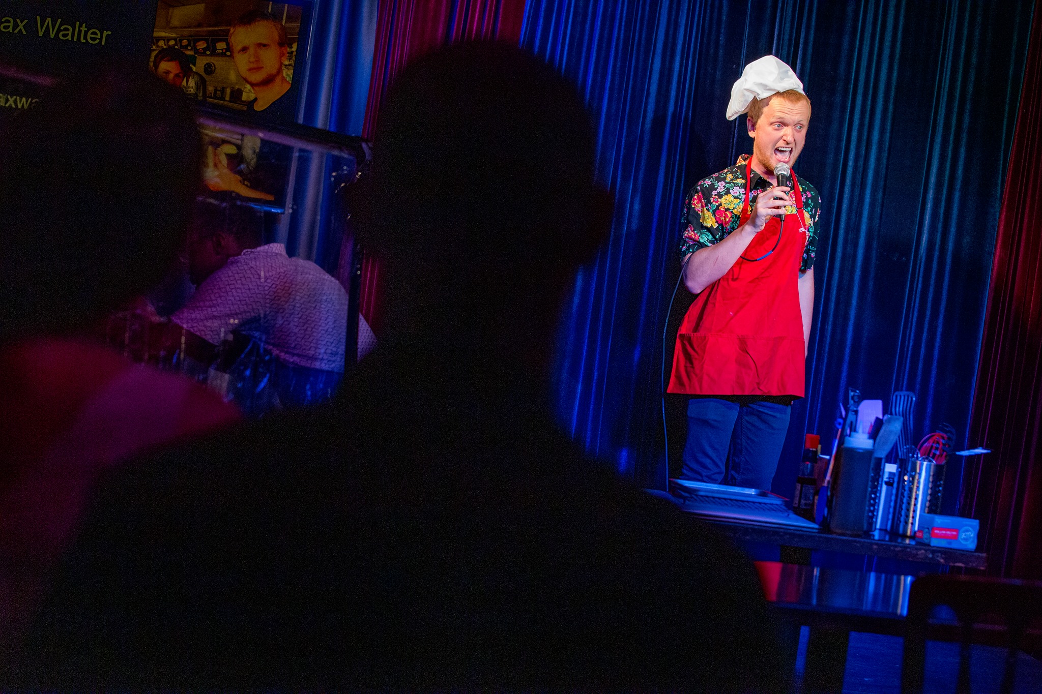 Chicago stand-up comedian, Max Walter, preforms live on stage at Sauteed Stand up, Chicago's premiere comedy cooking competition. The photographer has comedic timing, Max is pictured mid-joke with his mouth wide open and eyes popping out of his head while he grips a microphone.